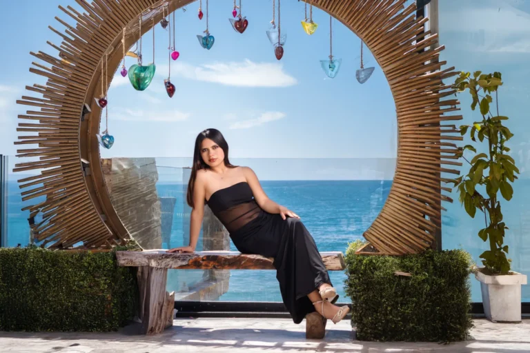Sesión de fotos de cumpleaños en Playas de Rosarito: joven con vestido negro sentada bajo un arco de madera frente al mar